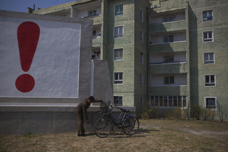 David Guttenfelder - A North Korean man checks his bicycle next to a painted exclamation point on a propaganda billboard on Wednesday April 24, 2013 in Kaesong, North Korea, north of the demilitarized zone which separates the two Koreas