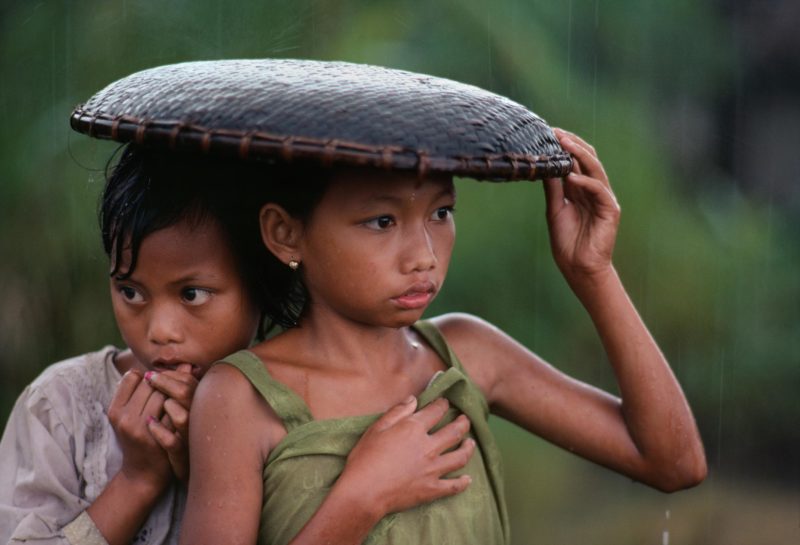 Steve McCurry - Indonesia. Java. 1983, Girls huddle under a rice basket to escape the rain