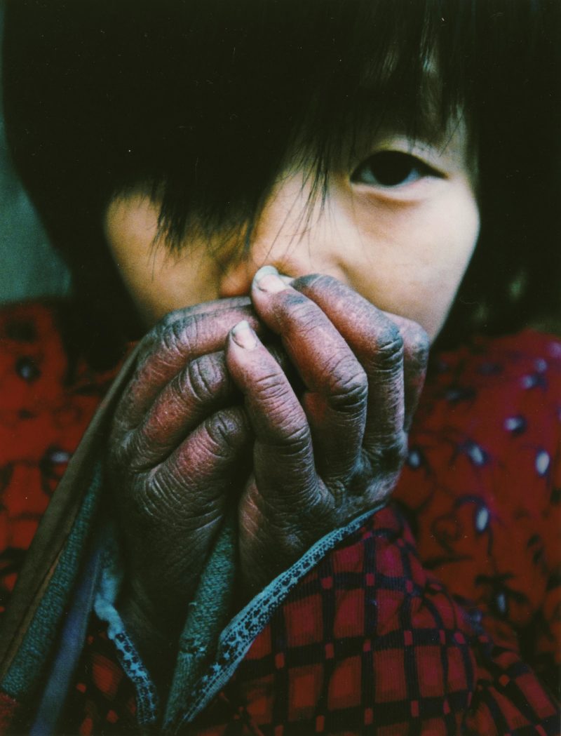 Lu Guang - A young girl warms her hands in winter. Her father is infected with HIV and still cares for five children and his elderly parents