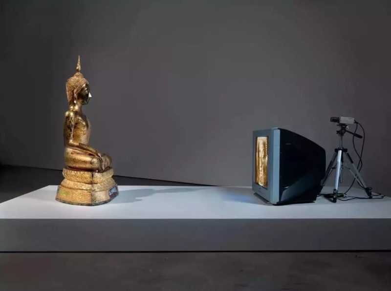 Nam June Paik - Golden Buddha, 2005, closed-circuit video (color) with television and wood Buddha with permanent oil marker additions, 46 1:2 × 106 × 31 3:4 inches (118.1 × 269.2 × 80.6 cm)
