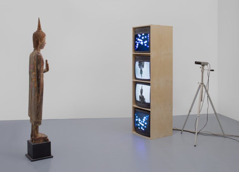 Nam June Paik - Standing Buddha with Outstretched Hand, 2005 Single-channel video (color, silent) with televisions, closed-circuit video (colour), and wood Buddha with permanent oil marker additions