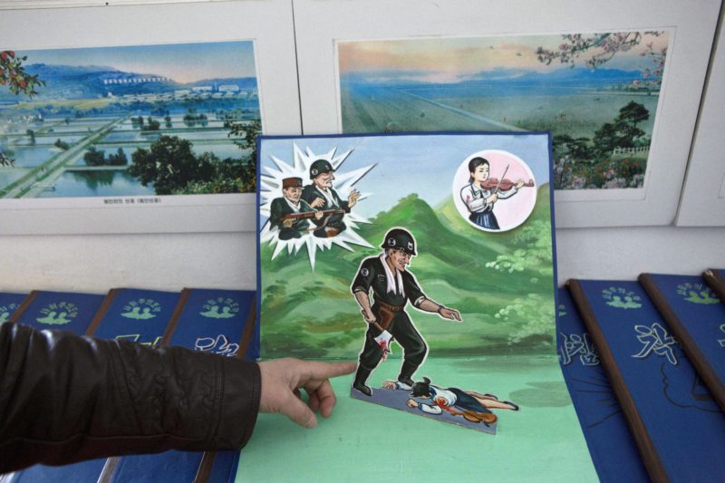 A North Korean teacher holds open a children's pop-up book, which depicts a U.S. soldier killing a Korean woman with a hatchet, in a library room at Kaeson Kindergarten in central Pyongyang on Saturday, March 9, 2013. For North Koreans, the systematic indoctrination of anti-Americanism starts as early as kindergarten.