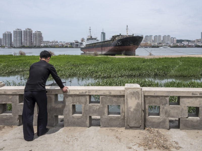 Carl De Keyzer - Sinuiju, North Pyong’an Province. Korean freighter moored on the Amnok (Yalu) River. Across the far bank is the Chinese city of Dandong, Liaoning Province. 9 June 2017 11:00 AM